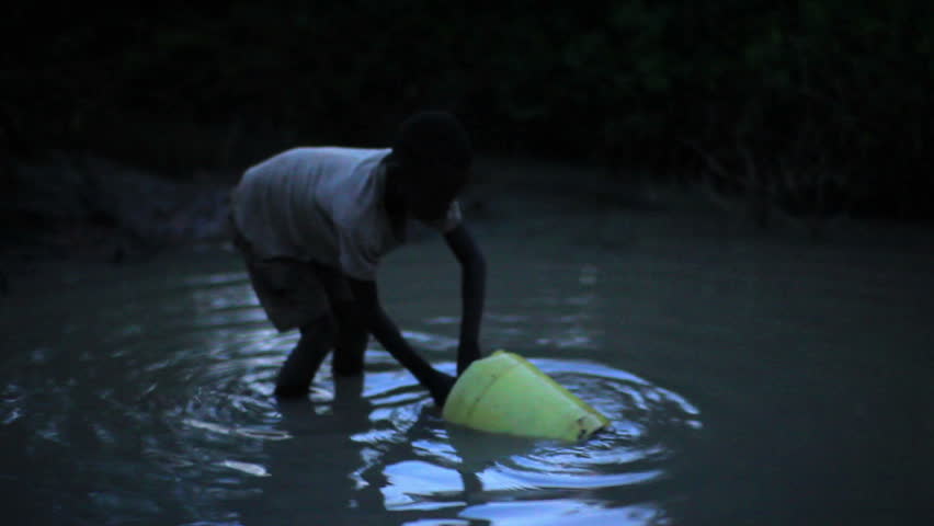 KENYA, AFRICA - CIRCA AUGUST 2010: Boy uses bucket to collect water from water hole at night in Africa circa August 2010.