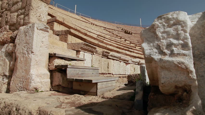 Dolly slider move up and over a boulder to reveal the theater seating at the ruins of Caesarea in Israel.