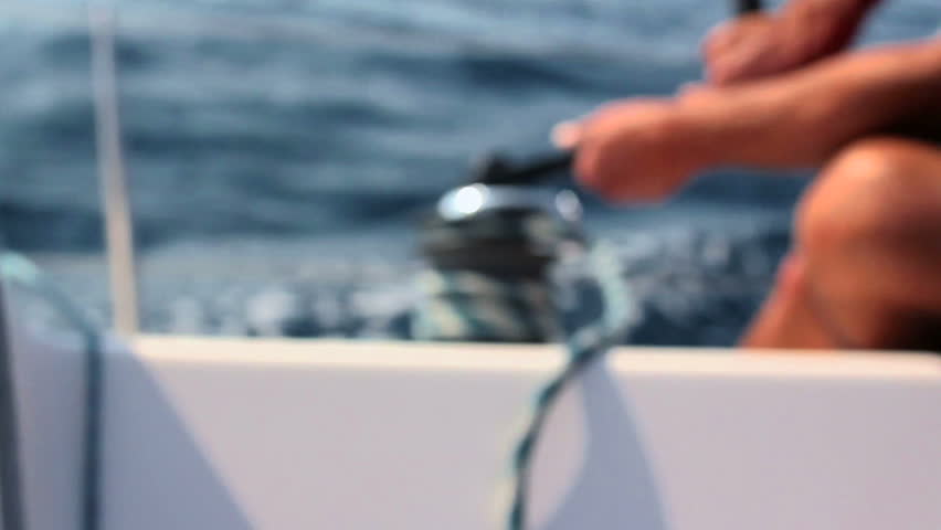 People sailing, man pulling ropes, winding sheets around winches