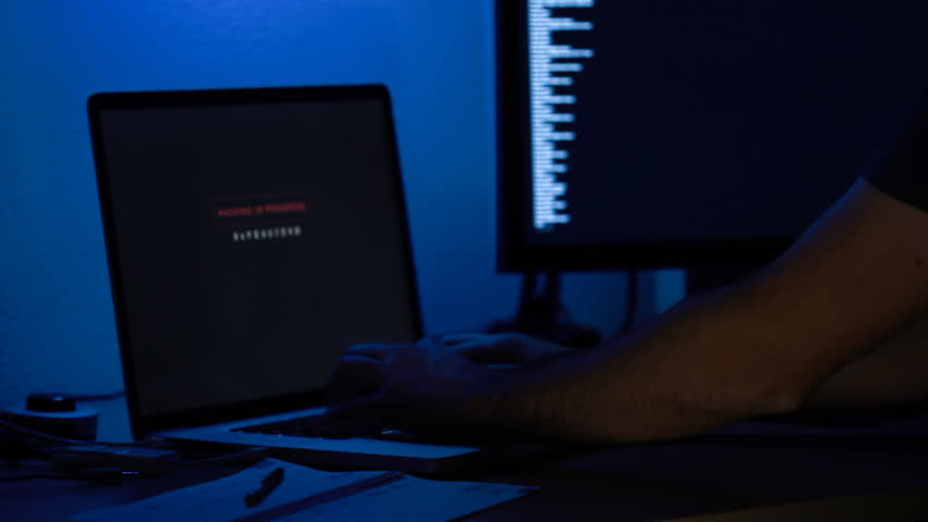 hacker at night in a dark blue illuminated office trying to breach into a computer system
