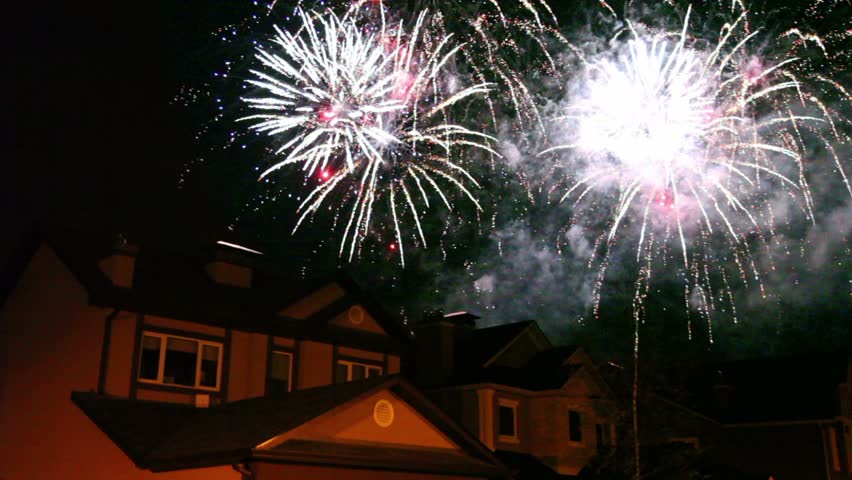 Fireworks glisten at dark sky over roofs of few houses