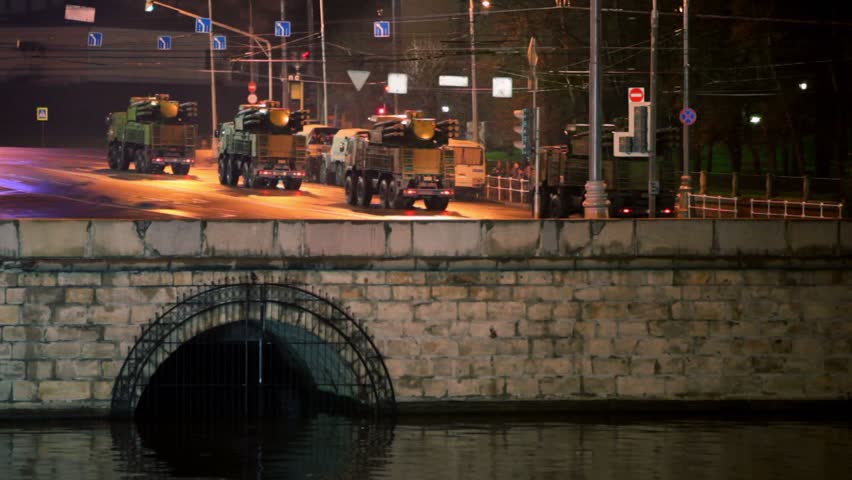 Military motorcade ride by quay at night, many soldiers stands at background