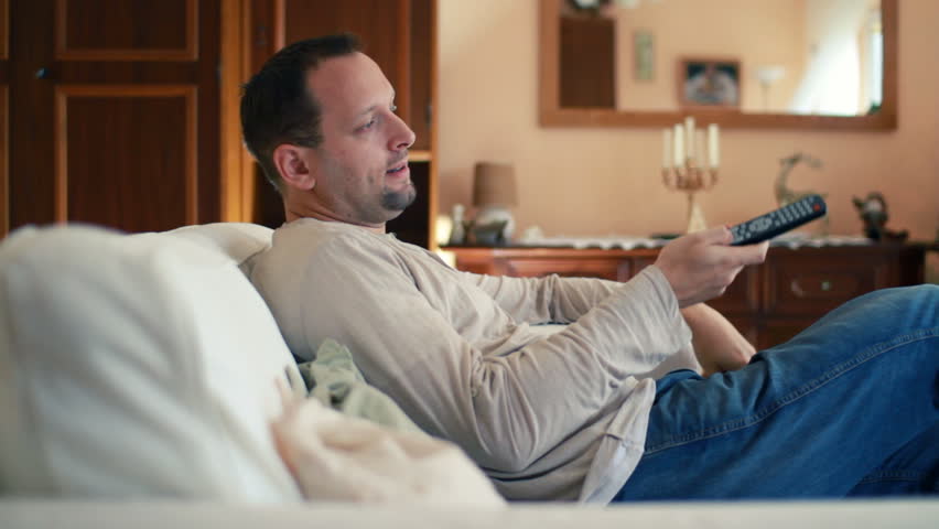 Young man with tv remote watching tv on sofa 