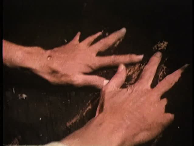 Close-up of hands removing soil from wooden coffin