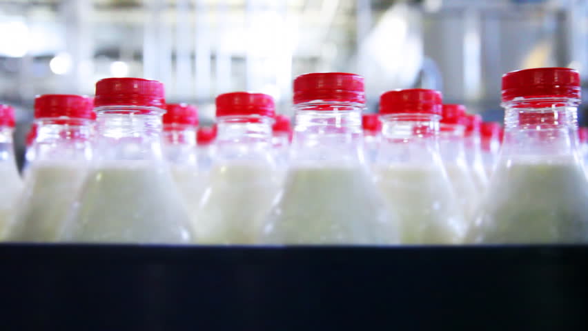 rows of plastic bottles with milk and red caps at factory, close-up