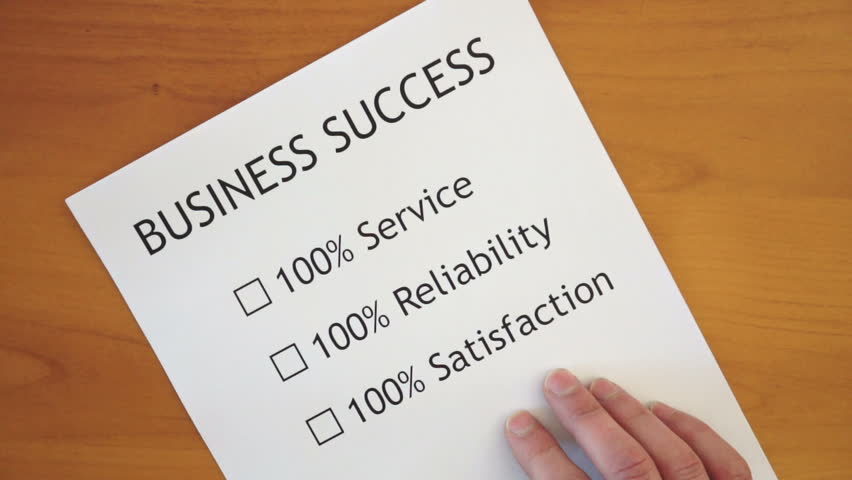 A man with a list printed on a piece of paper sitting on a table checks off 100% Service, 100% Reliability and 100% Satisfaction on a list that's titled Business Success.