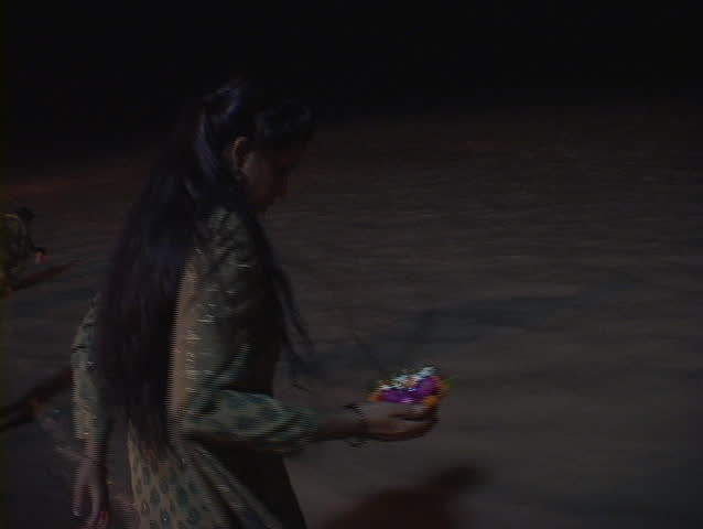 A woman puts a small aarti, floating offering, into the Ganges River at night.