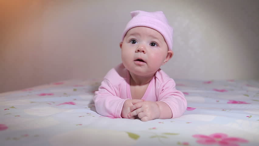 A cute little baby lying on her stomach and wearing a pink hat.