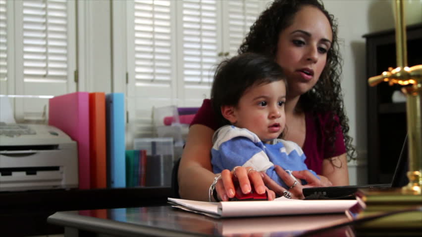 A cute little toddler sits in his mother's lap as she works in her home office.