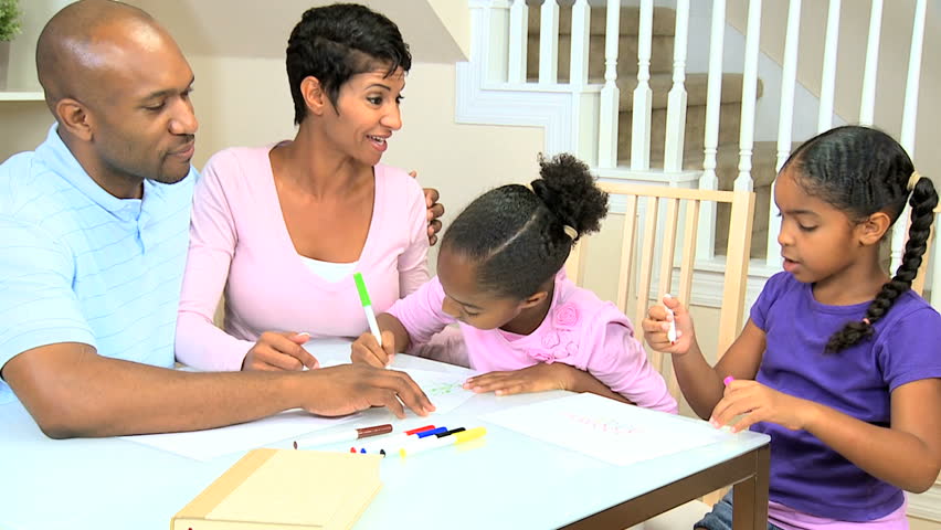 Young ethnic parents watching their young daughters using coloring crayons