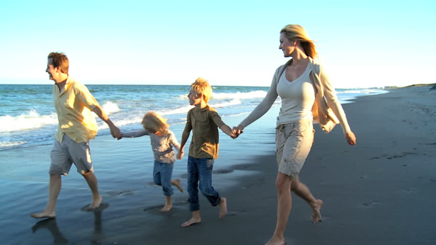 Happy young family group walking along the beach at dusk