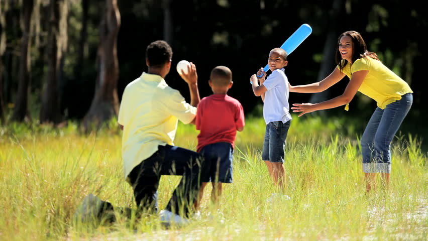 Attractive young african american family playing baseball together on parkland