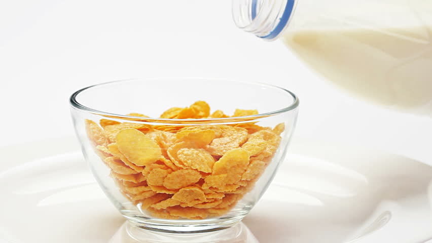 Corn flakes in a glass bowl pouring with milk over white