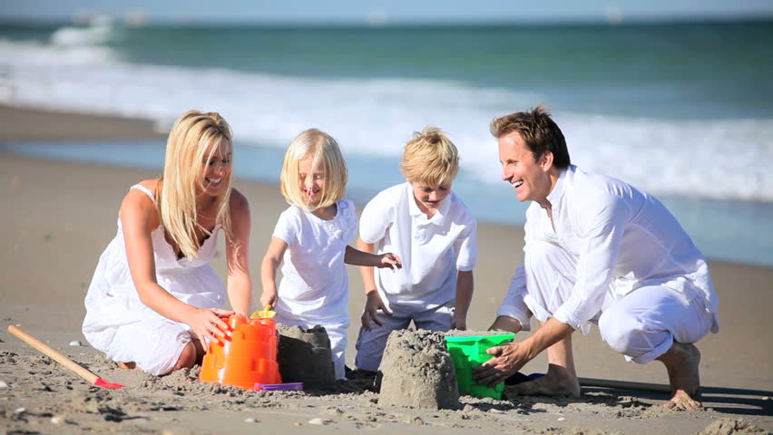 Happy caucasian children and parents having fun on the beach building sand castles