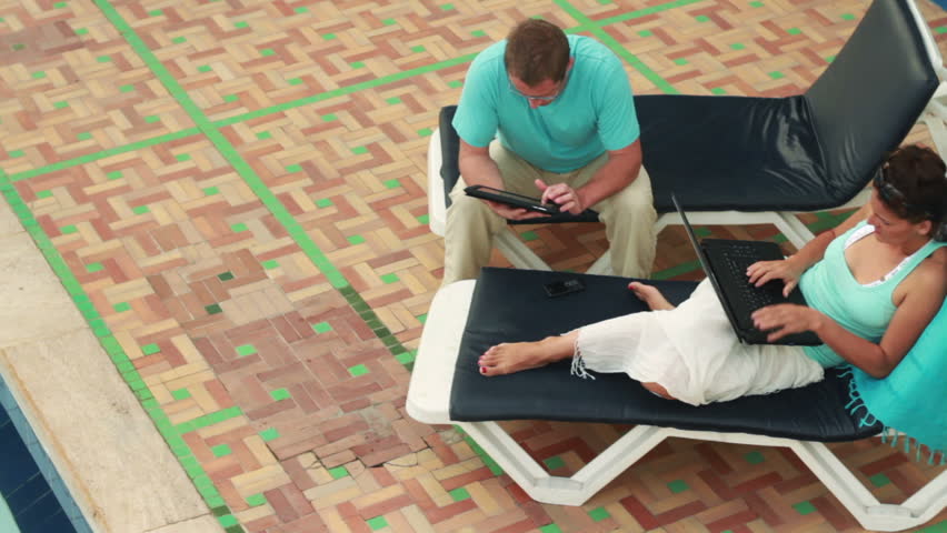 Couple with tablet computer and laptop relaxing on sunbeds, dolly shot 