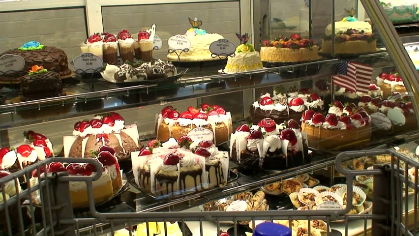 A man looking over a grocery case full of beautifully decorated cakes