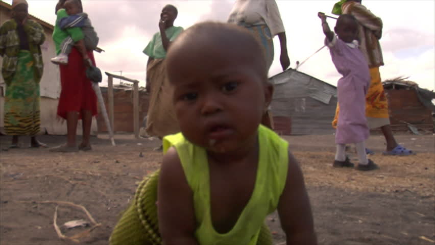 Kenya - Circa 2006: Unidentified little baby on all four's stares into camera, crawls toward it, and reaches hand out to touch camera, unidentified people stand in background circa 2006 in Kenya.