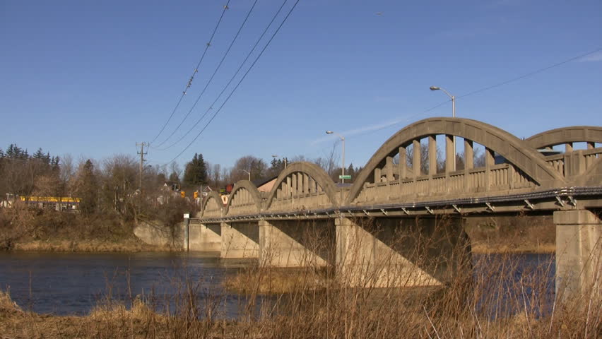 An old two lane concrete bridge crosses over the Grand River.  The river is gently flowing as the sun illuminates the bridge. Birds are sitting on some powerlines above the bridge. (High Definition)