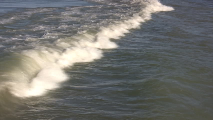 Waves continuously roll along as they make their way to the shore.  The sun illuminates the surf.  (High Definition)