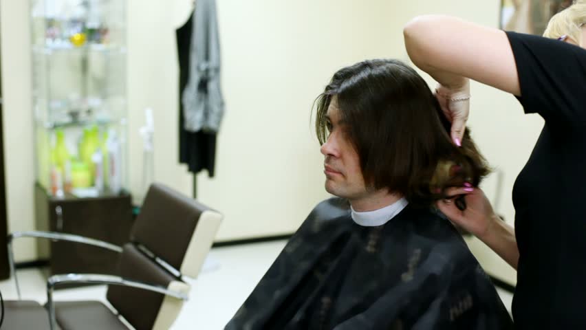 Young man sits in hairdressing salon in seat and gets his hair done