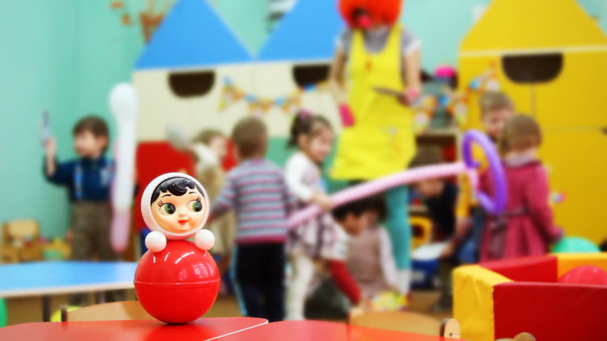 roly-poly toy on table, then focus moved to children playing with clown in kindergarten