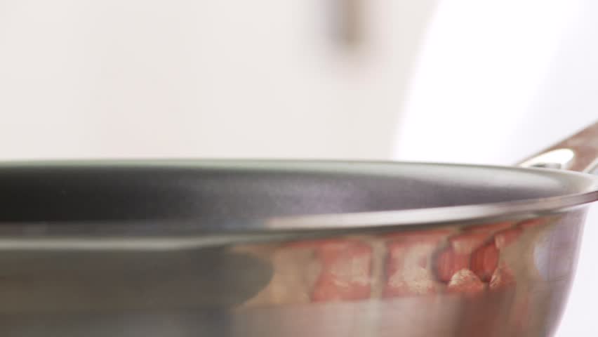 A piece of butter being placed in a pan with a raw burger