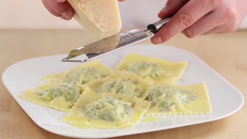 Cooked ravioli being sprinkled with Parmesan cheese