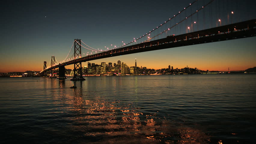 Aerial sunset low angled water view under the illuminated two levels of Oakland Bay Bridge, San Francisco, America