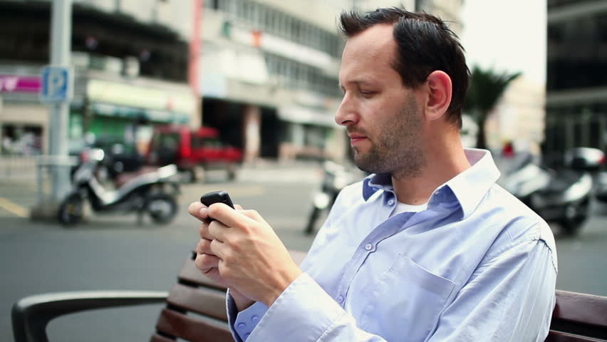 Handsome young man using smartphone by the city street

