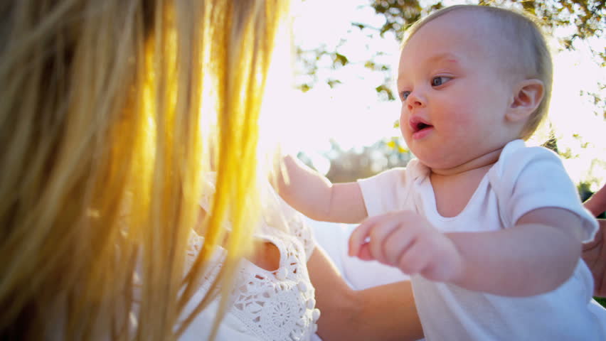 Young caucasian mother bouncing her baby in the sunshine outdoors
