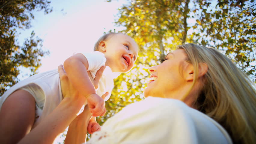 Young blonde mother and baby laughing together playing outdoors