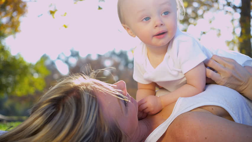 Beautiful young mother in close up lying outdoors on the grass and tenderly kissing her baby