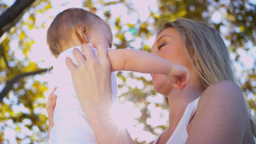 Beautiful young blonde mother bouncing her young baby in her arms outdoors