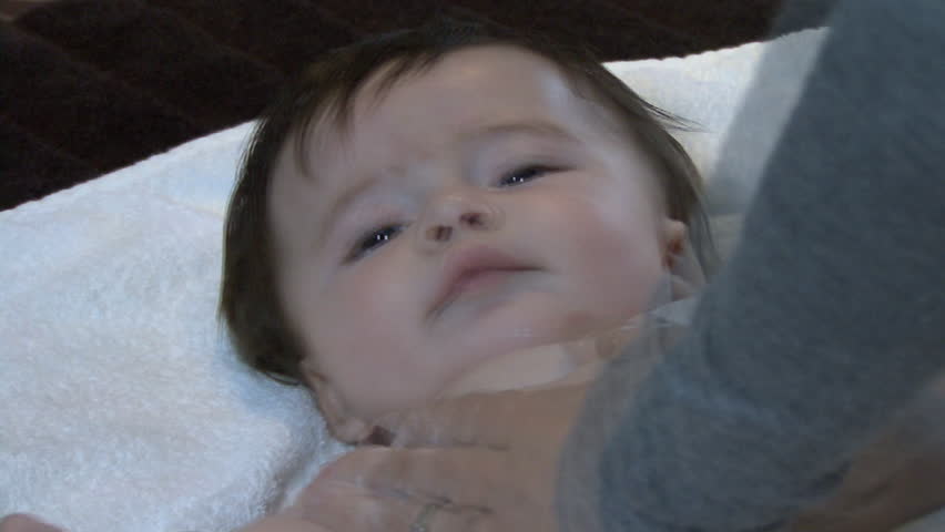MEDIUM CLOSE UP PAN OF A MOTHER APPLYING LOTION TO HER BABIES TORSO