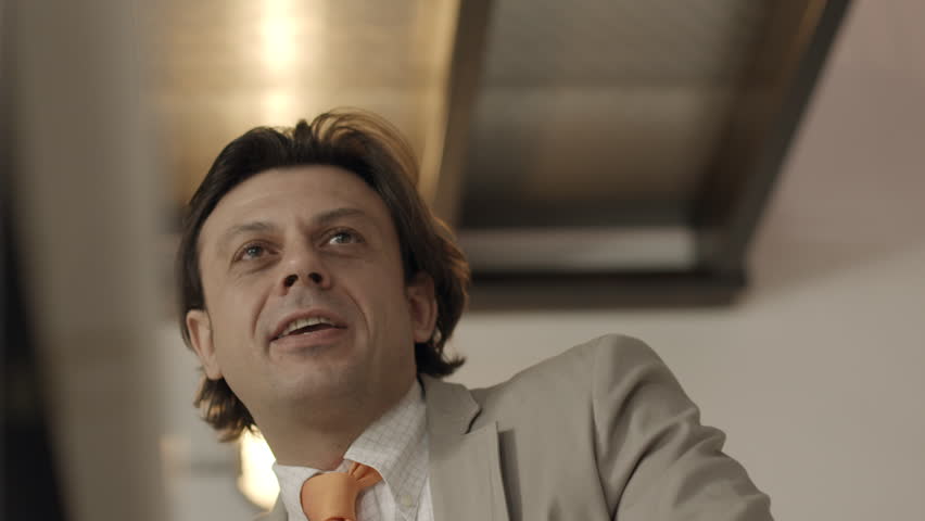 Adult businessman at work in office, talking to co-worker and smiling at business meeting. Low angle view