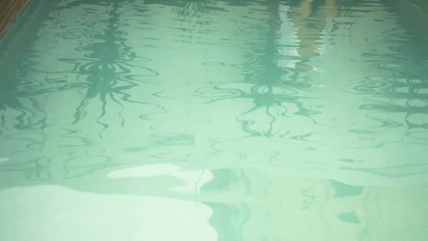 LONG SHOT PAN OF A MAN DIPPING HIS FEET IN A POOL