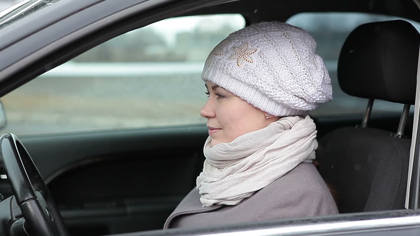 Pretty young Caucasian woman showing ignition key, starting the car and driving away.