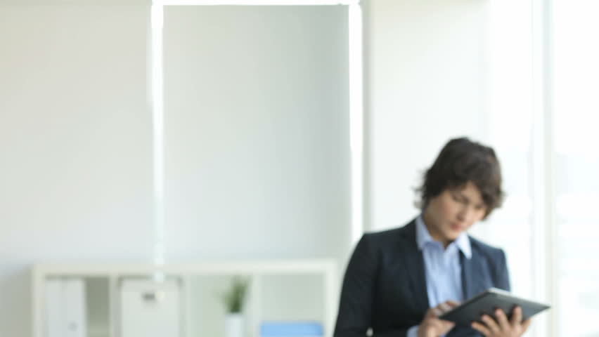 Handsome businessman talking on the phone, his colleague in the background working on her tablet computer