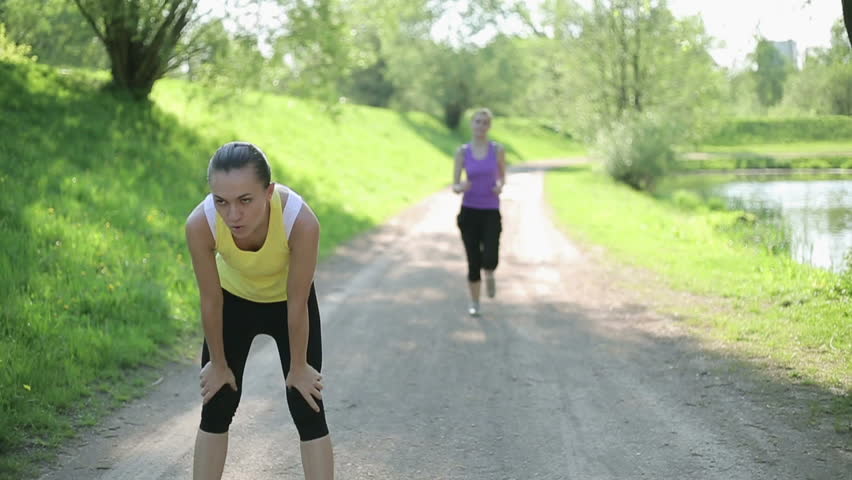 Two young women jogging in the park, 
One woman taking breath during jogging, slow motion