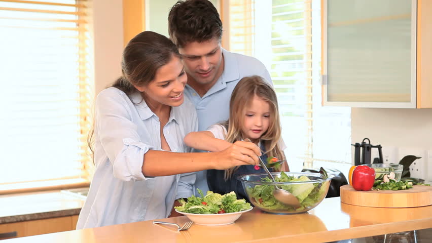 Family in the kitchen making a salad together and tossing it