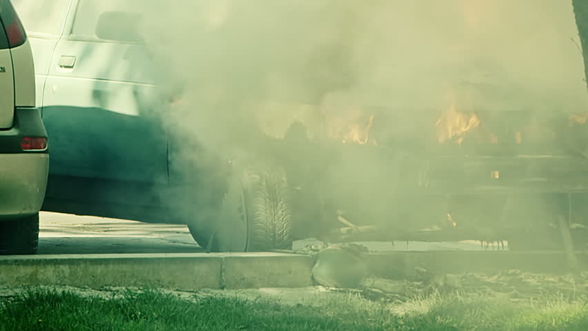 Car engulfed in flames with lot of smoke. A man tries to extinguish the fire with extinguisher 