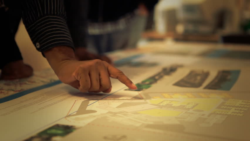 A dolly track close up shot of a hand pointing at detail in blueprint.