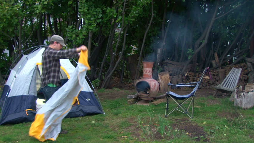 Man sets up campsite with tent and makes fire in backyard with his pet cats interested in the activity.