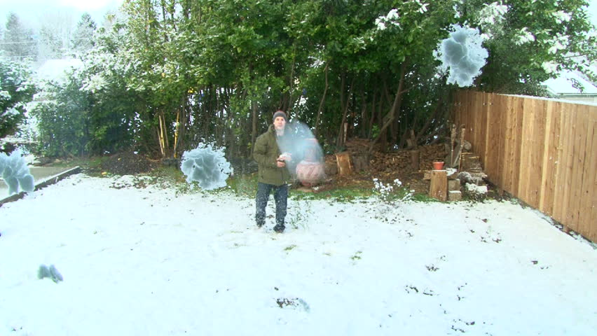 Man in winter clothes runs out to backyard after snowfall and throws snowballs at camera lens, then wipes glass clean.