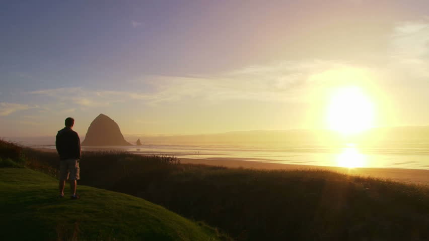 Man at Pacific Ocean near Cannon Beach looks out to sea as sun sets on beautiful day.