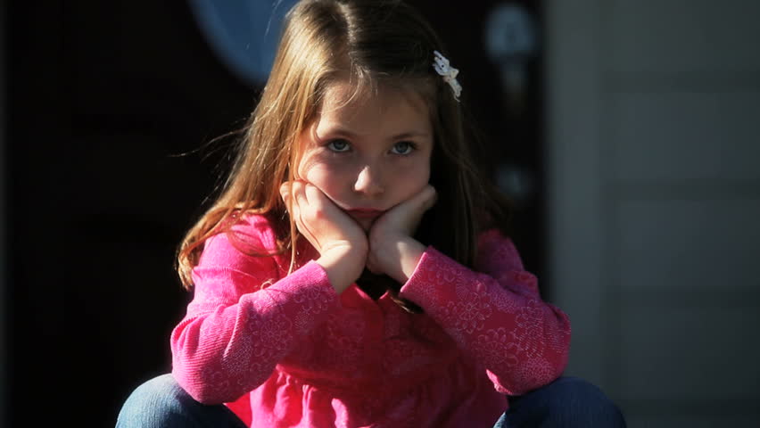 Little girl sitting in front of house with bored expression