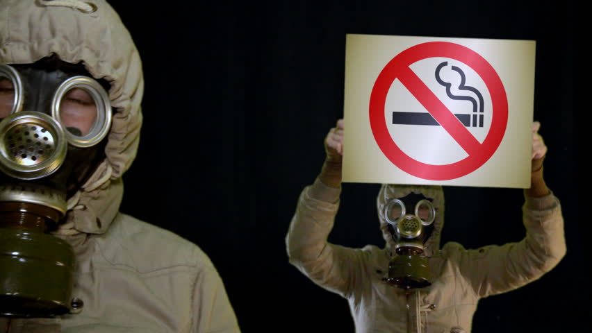 Peoples in gas mask holds anti-smoking sign
