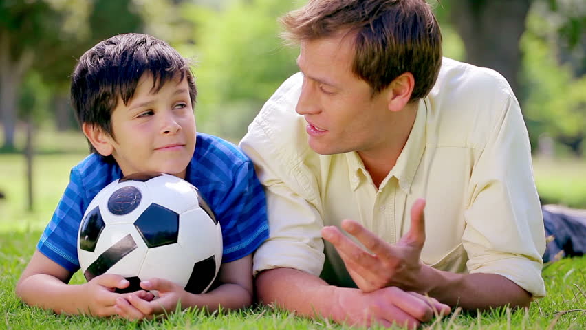 Happy father and son lying on the grass with a soccer ball in the countryside