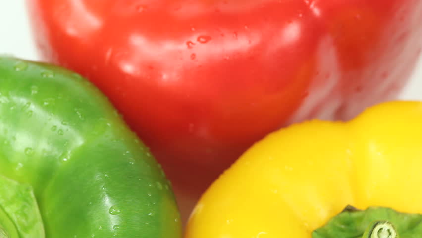 High angle shot of three colorful bell peppers revolving slowly on white background. Green, Yellow and Red paprika vegetable sprinkled with drops of water to make them even more tasty and appealing.