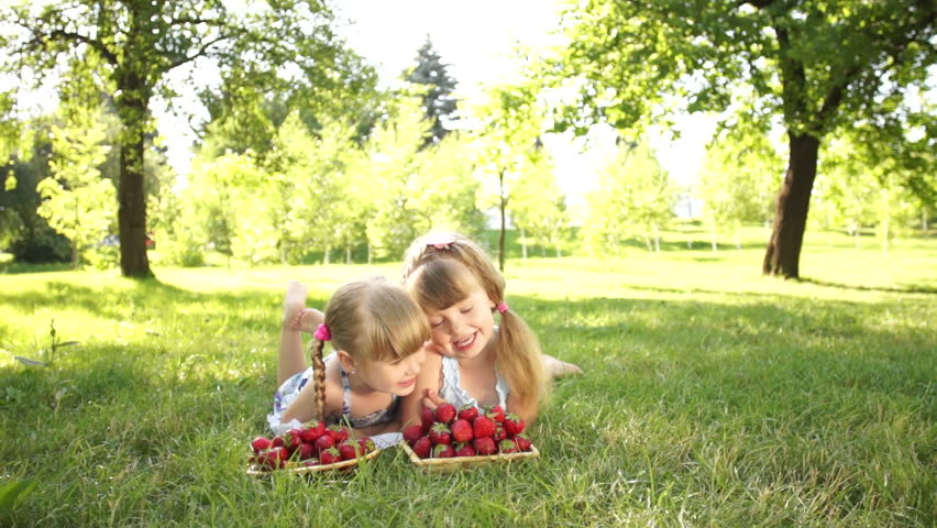 Laughing children lie on the grass. They eat strawberries
